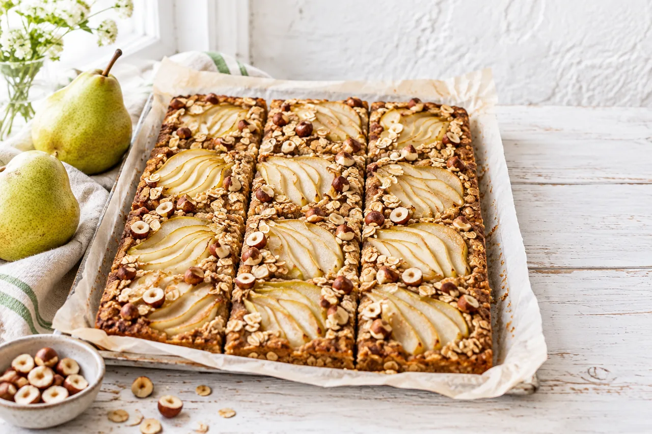 Birnen-Hafer-Kuchen vom Blech mit Birnenfächern und Haselnüssen auf hellem Holz im Tageslicht