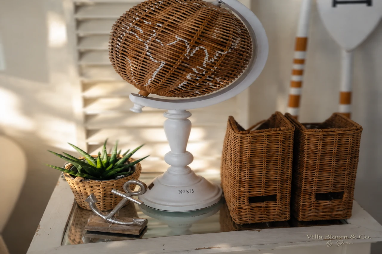Rattan-Globus, Weidenkörbe und kleine Sukkulente auf weißem Beistelltisch im Landhausstil